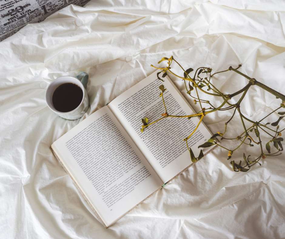 Un libro aperto sul letto con di fianco una tazza di caffè lungo e un ramo d'albero